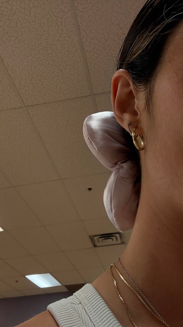 woman displaying a pink silk matbloom flower scrunchie in a studio on a black mat